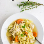 Chicken noodle soup in a white bowl with a title text overlay for Pinterest.
