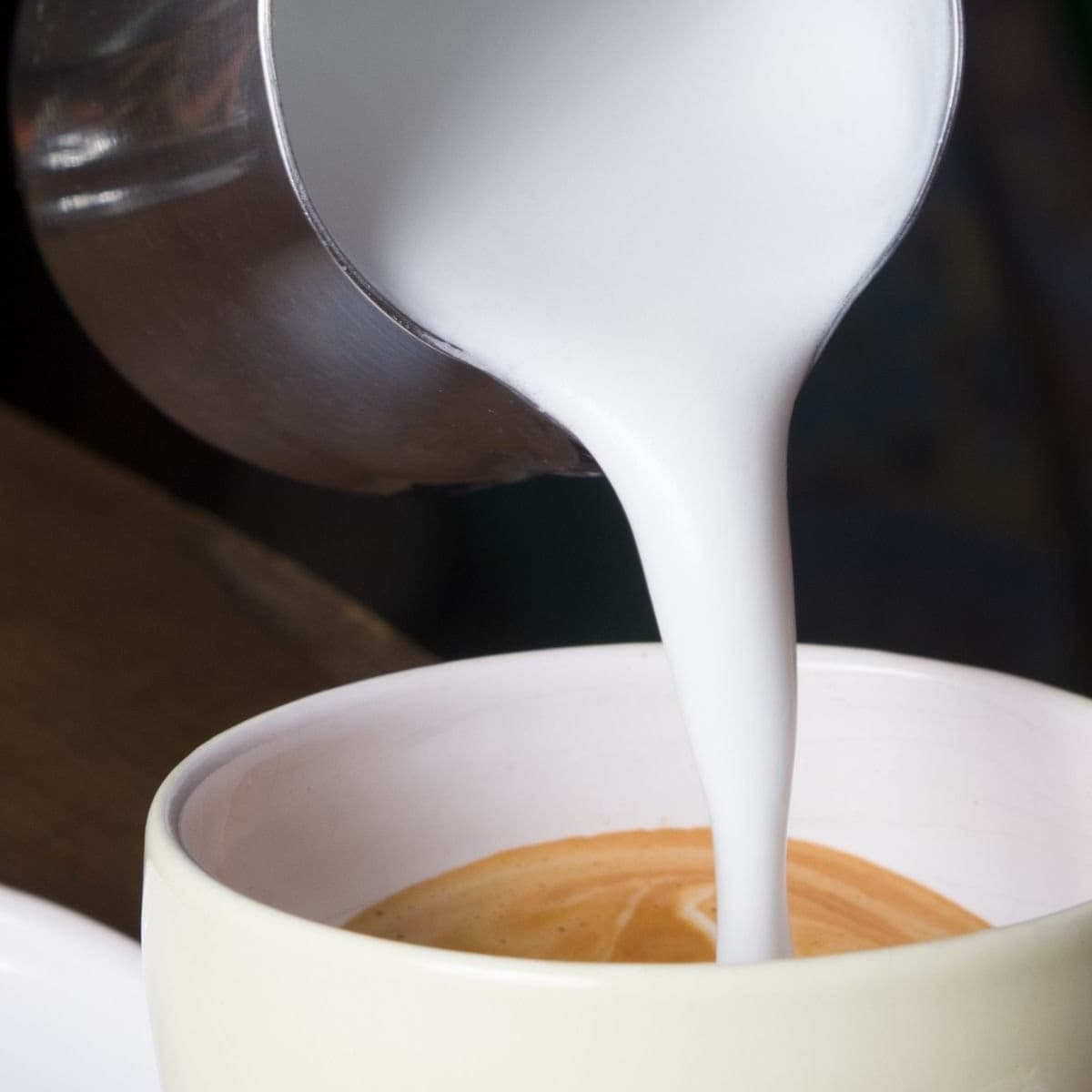 Hot, foamy milk being poured into a cup of coffee.
