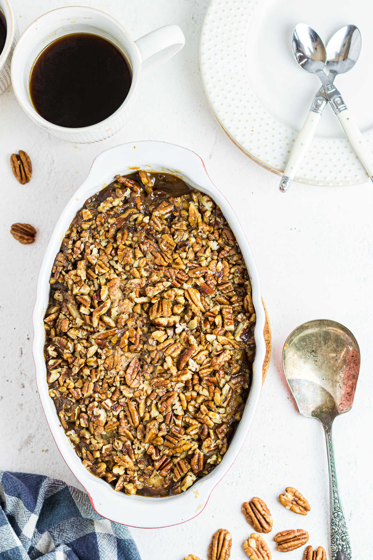 An overhead photo of pecan pie cobbler in a baking dish with a serving spoon and pecans around the border.