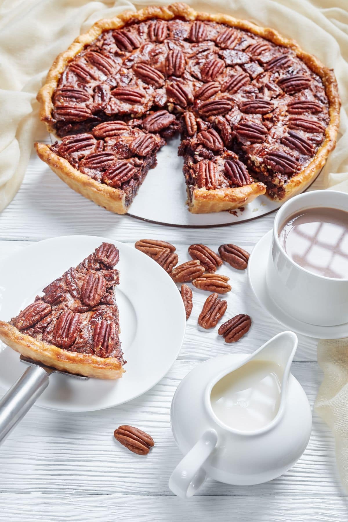 A pecan pie being cut and served with a cup of hot cocoa.