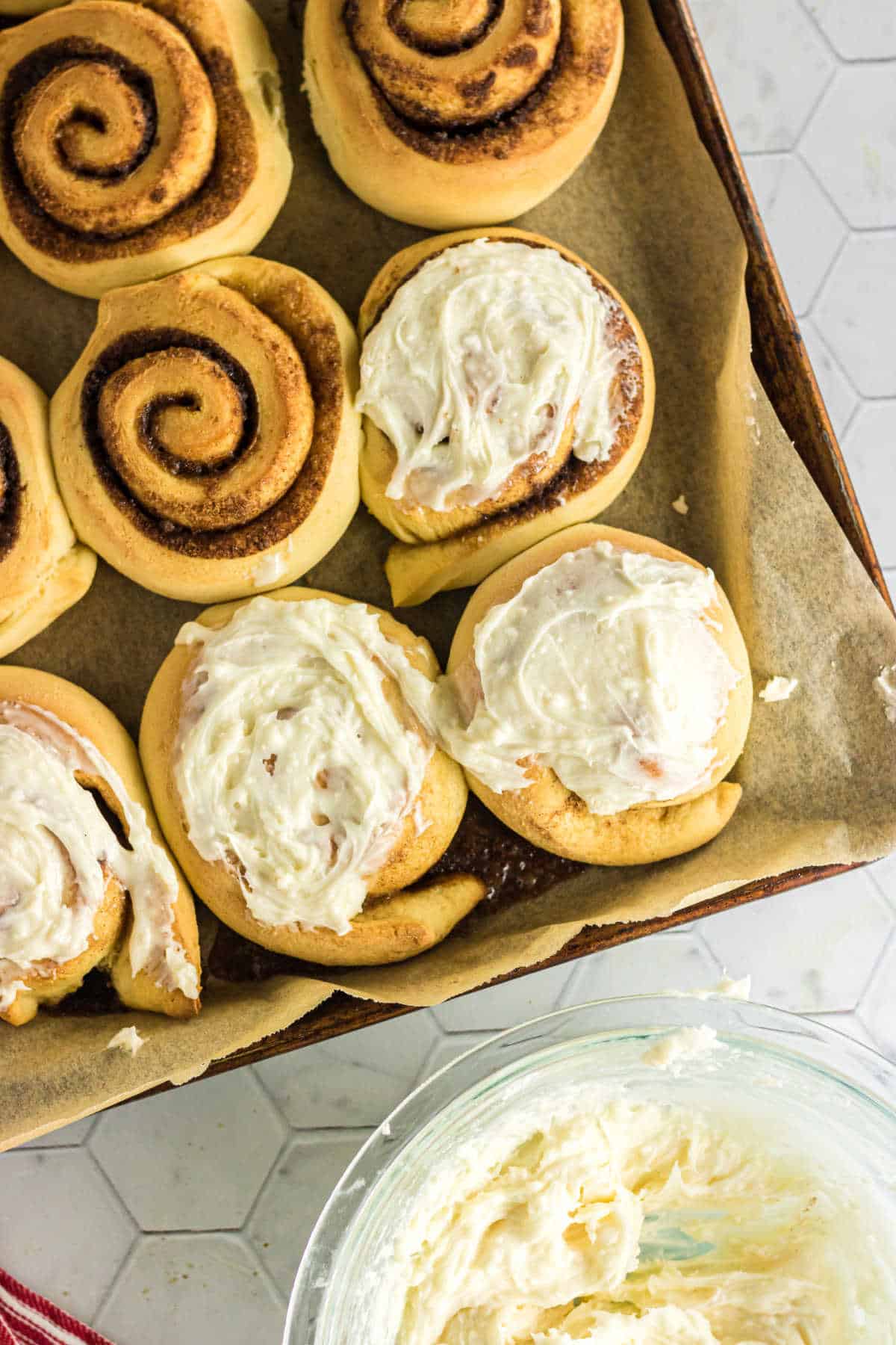 Finished sour cream cinnamon rolls being frosted with the creamy white icing.