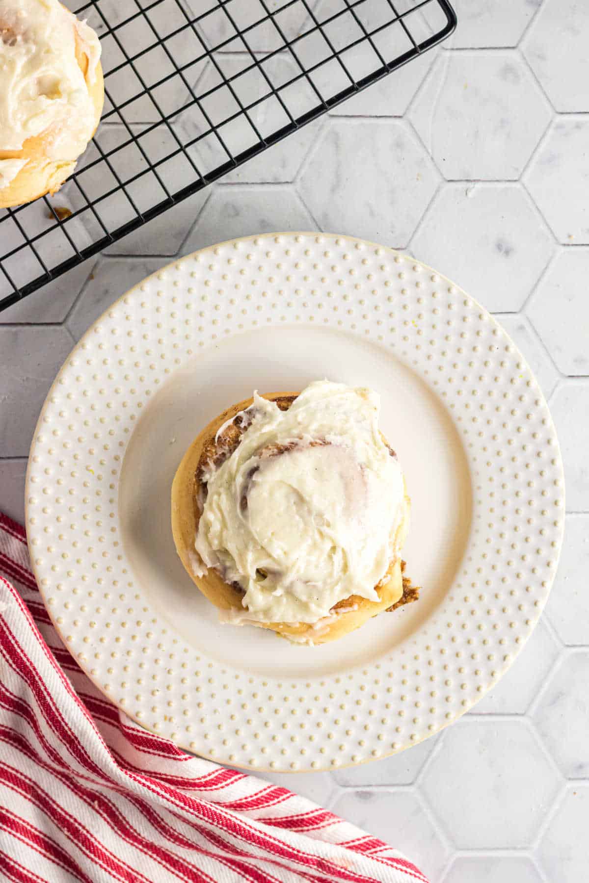 A cinnamon roll with thick, creamy white frosting on a white plate.