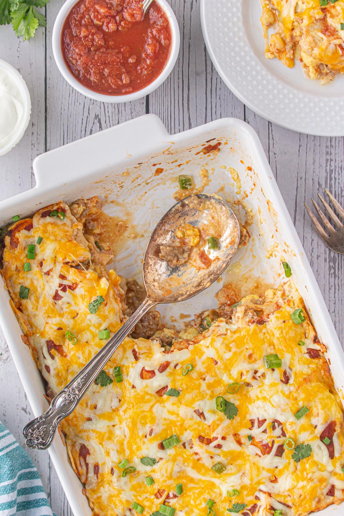 A baking dish full of breakfast burrito casserole, missing one portion that's on a plate off to the edge of the photo. 
