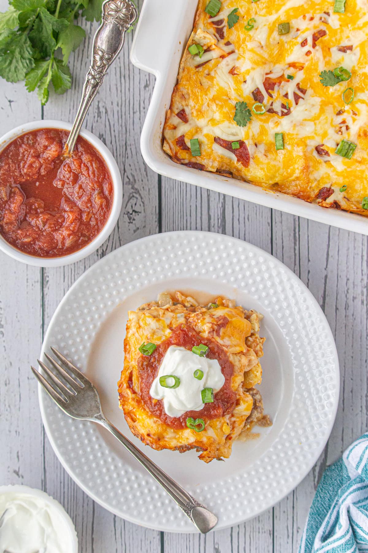 A plate with a large serving of breakfast burrito casserole next to a bowl of salsa.