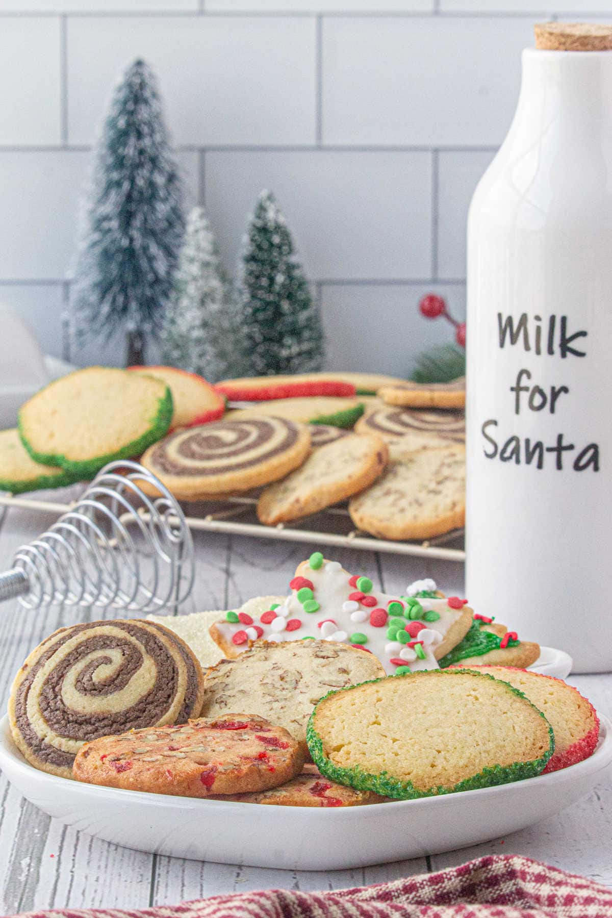 Various Christmas cookies on a white plate, including a swirled cookie, a sprinkled cookie, and a cookie with nuts and cherries.