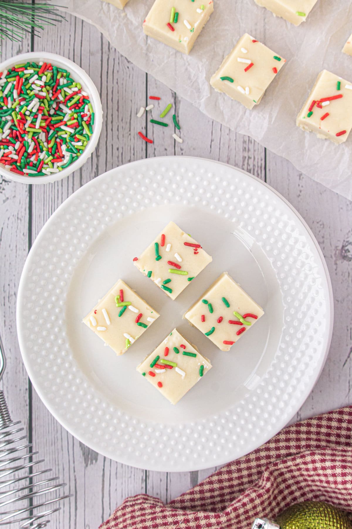 An overhead photo of white fudge with Christmas sprinkles on a white plate.