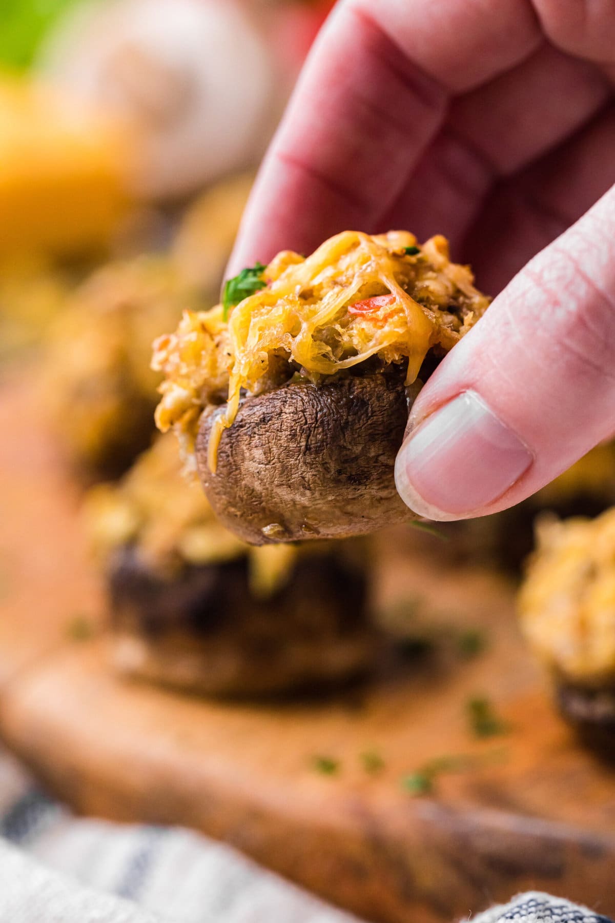 An up-close photo of a hand holding a stuffed mushroom. The other mushrooms are in the background of the photo.