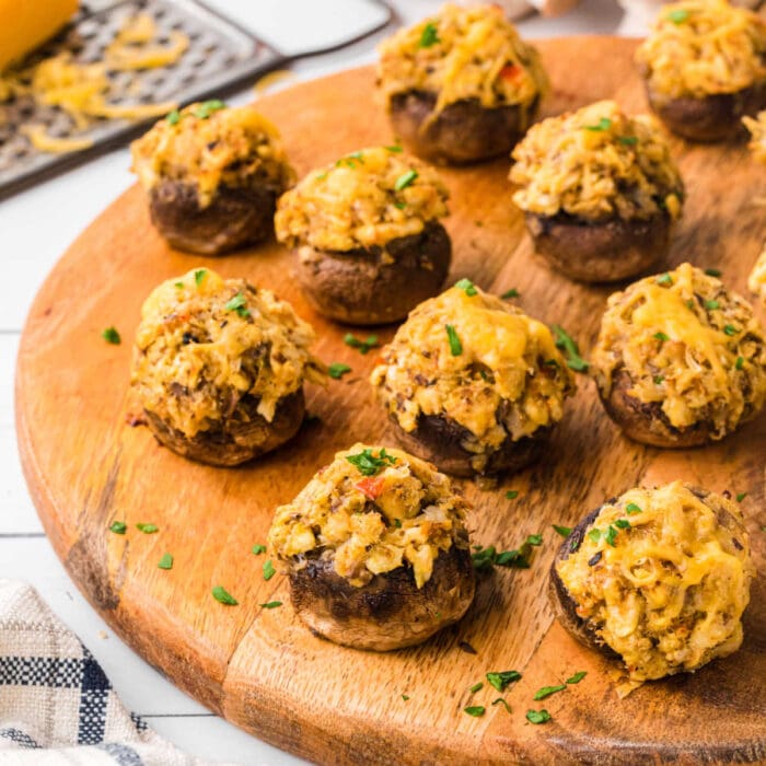 Crab stuffed mushrroms with melty cheese on top served on a wooden board.