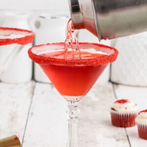 Red cocktail being poured into a martini glass.