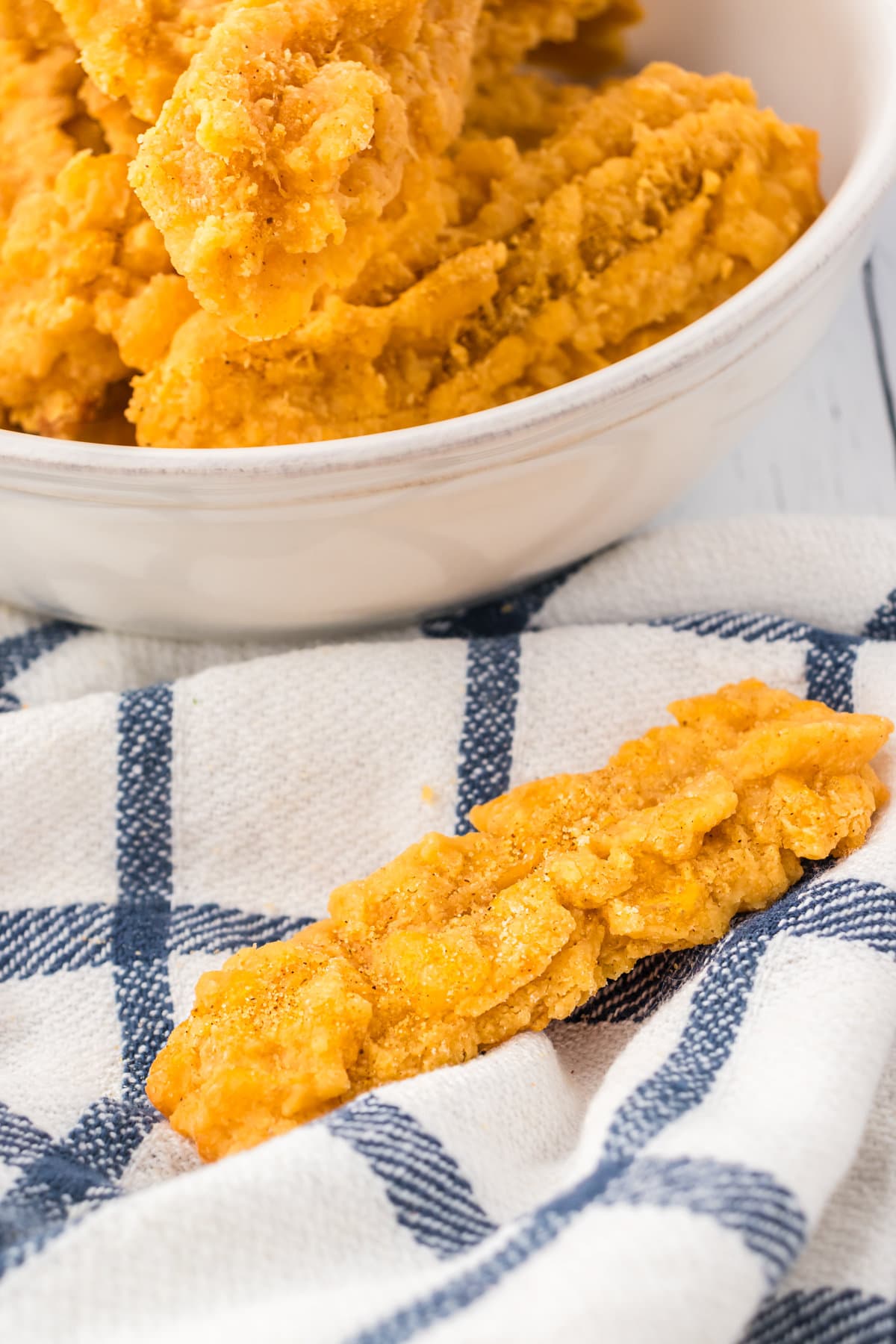 An up-close photo of a crispy cheese straw, next to a bowl with cheese straws.