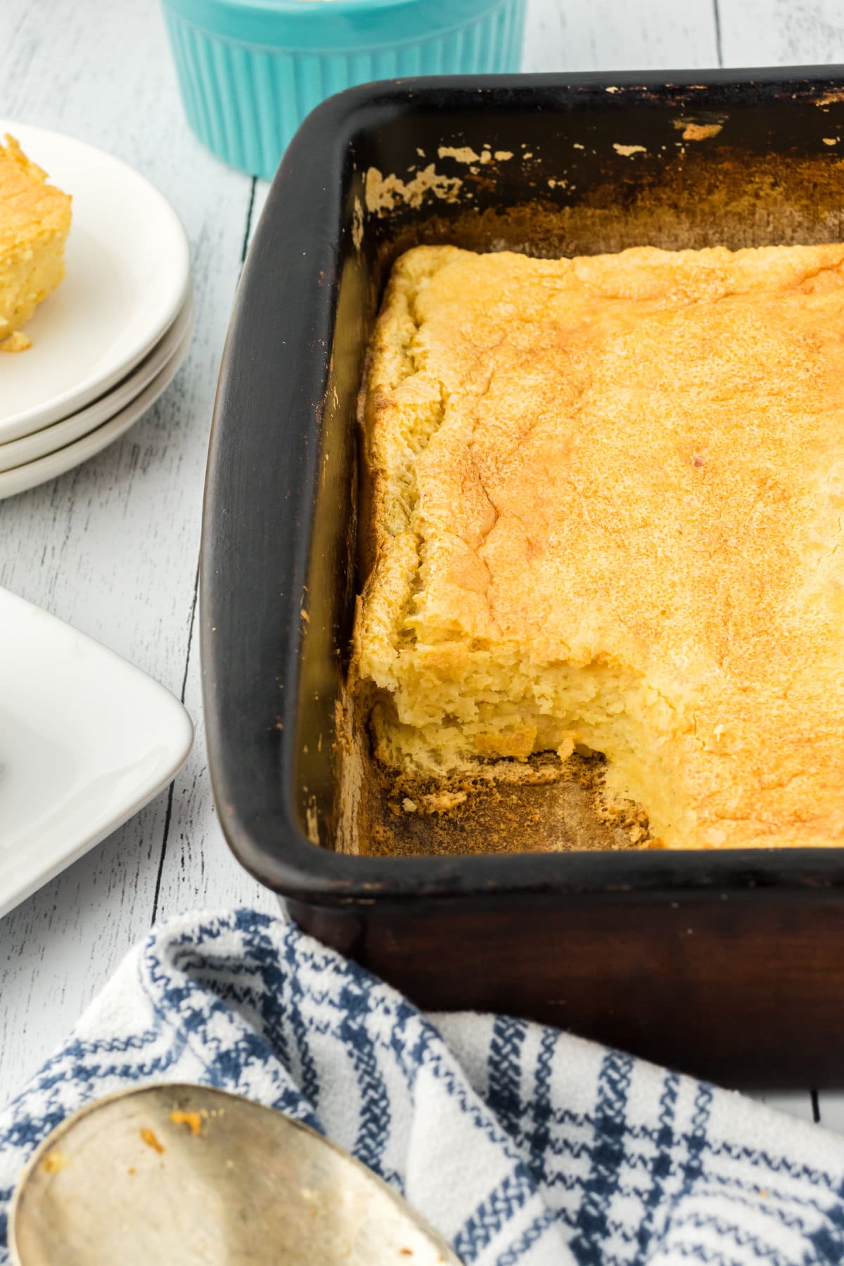 A baking dish with Southern spoon bread. A scoop has already been removed from the dish and sits on a plate out of focus of the camera frame.