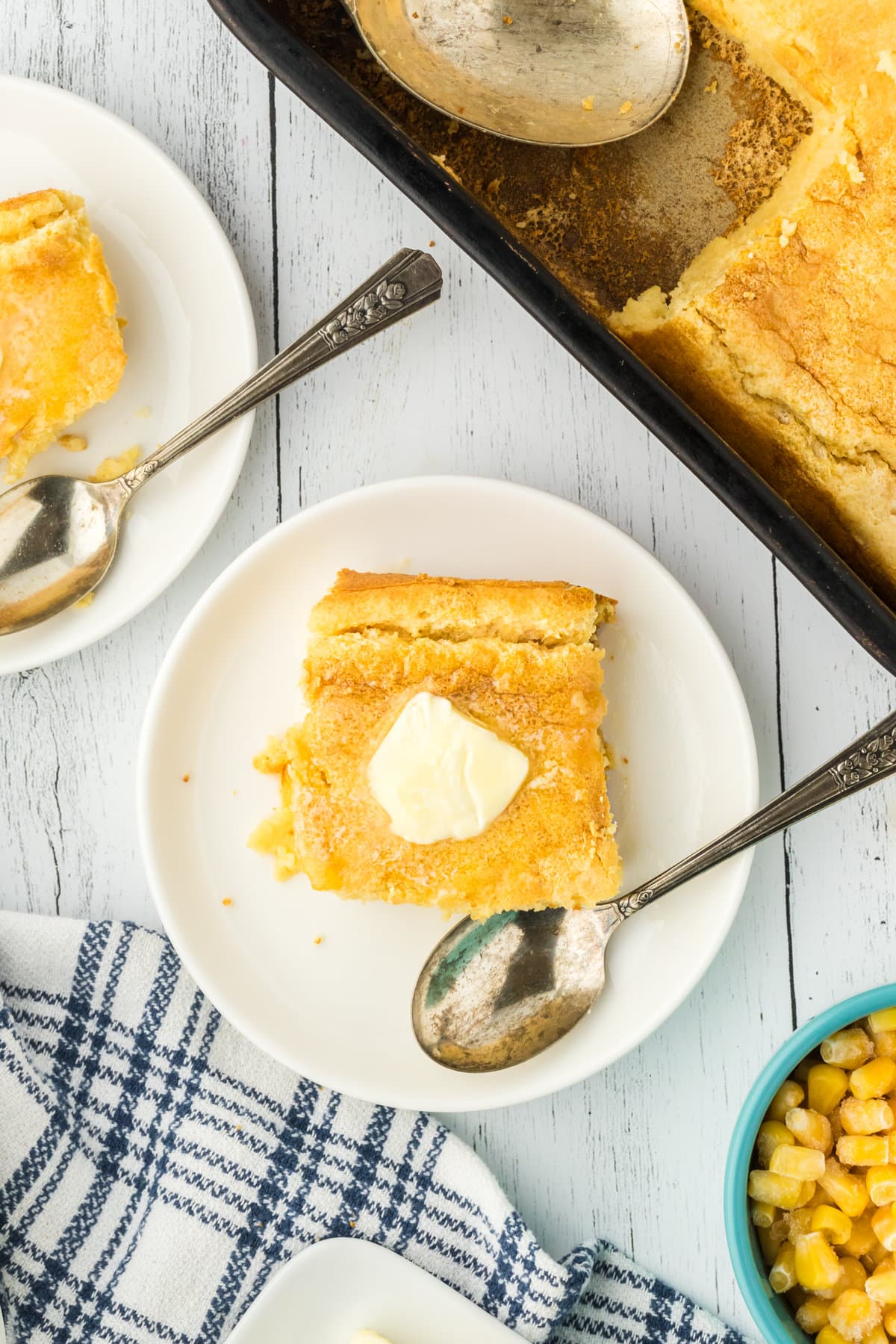 A portion of Southern spoon bread on a plate next to a spoon, topped with a melting pat of butter.