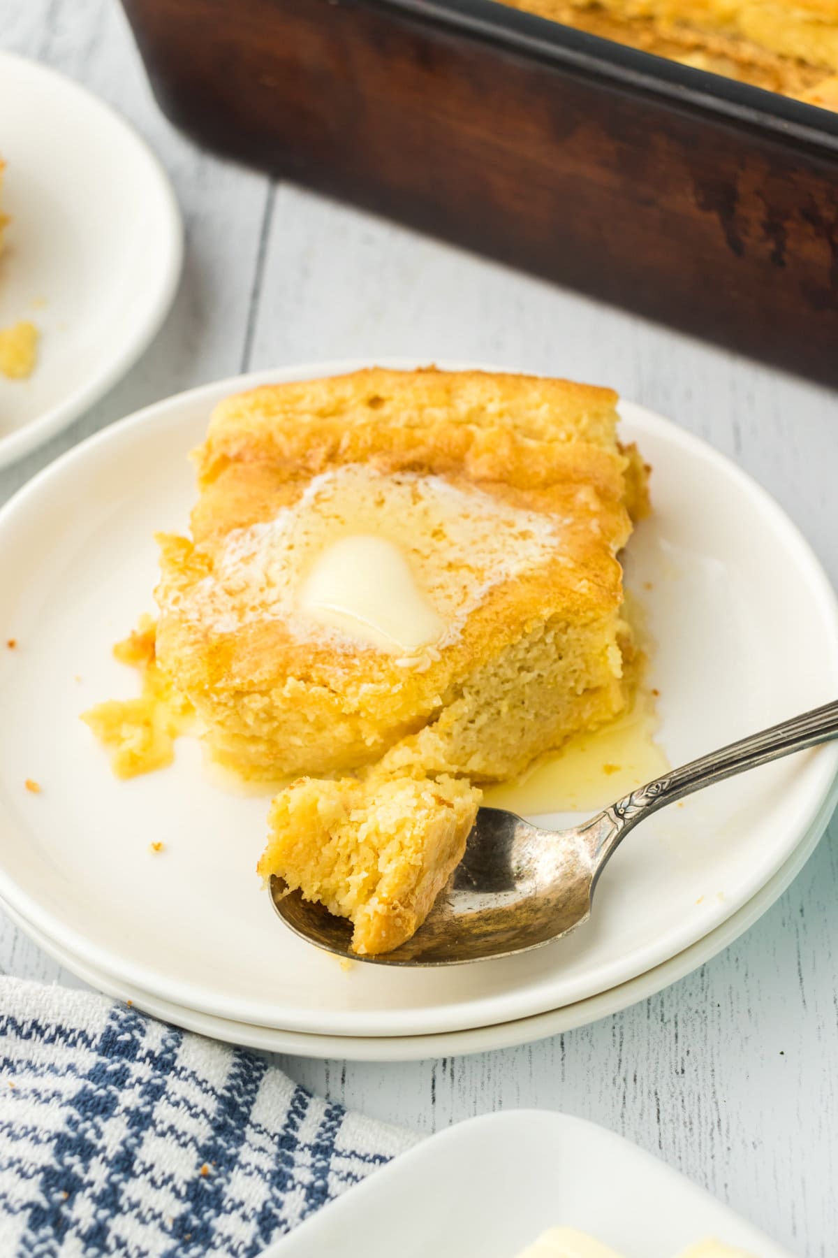 A plate of Southern spoon bread topped with melting butter. A spoon is scooping out a bite.