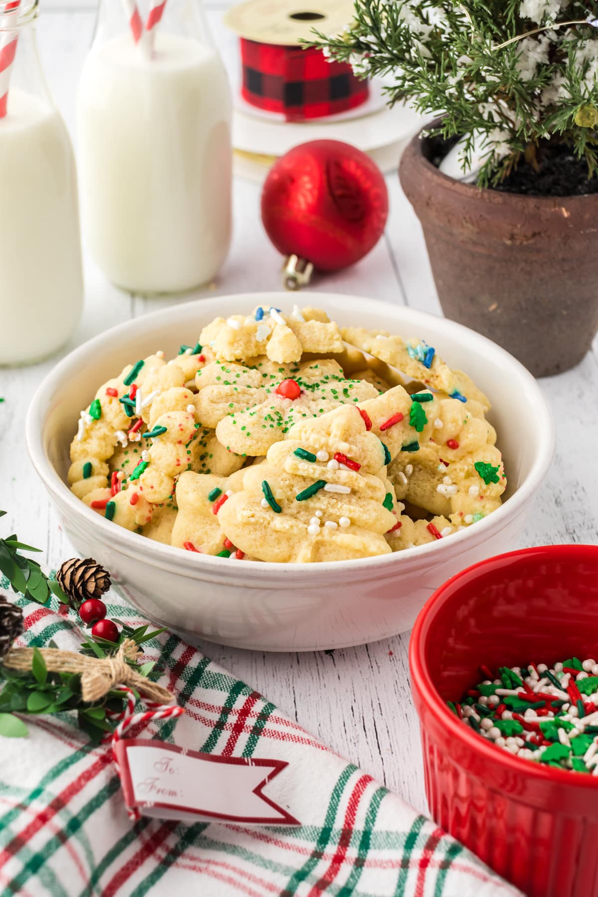 A white bowl filled with Christmas sprinkle-covered Spritz cookies shaped as Christmas trees and wreaths.