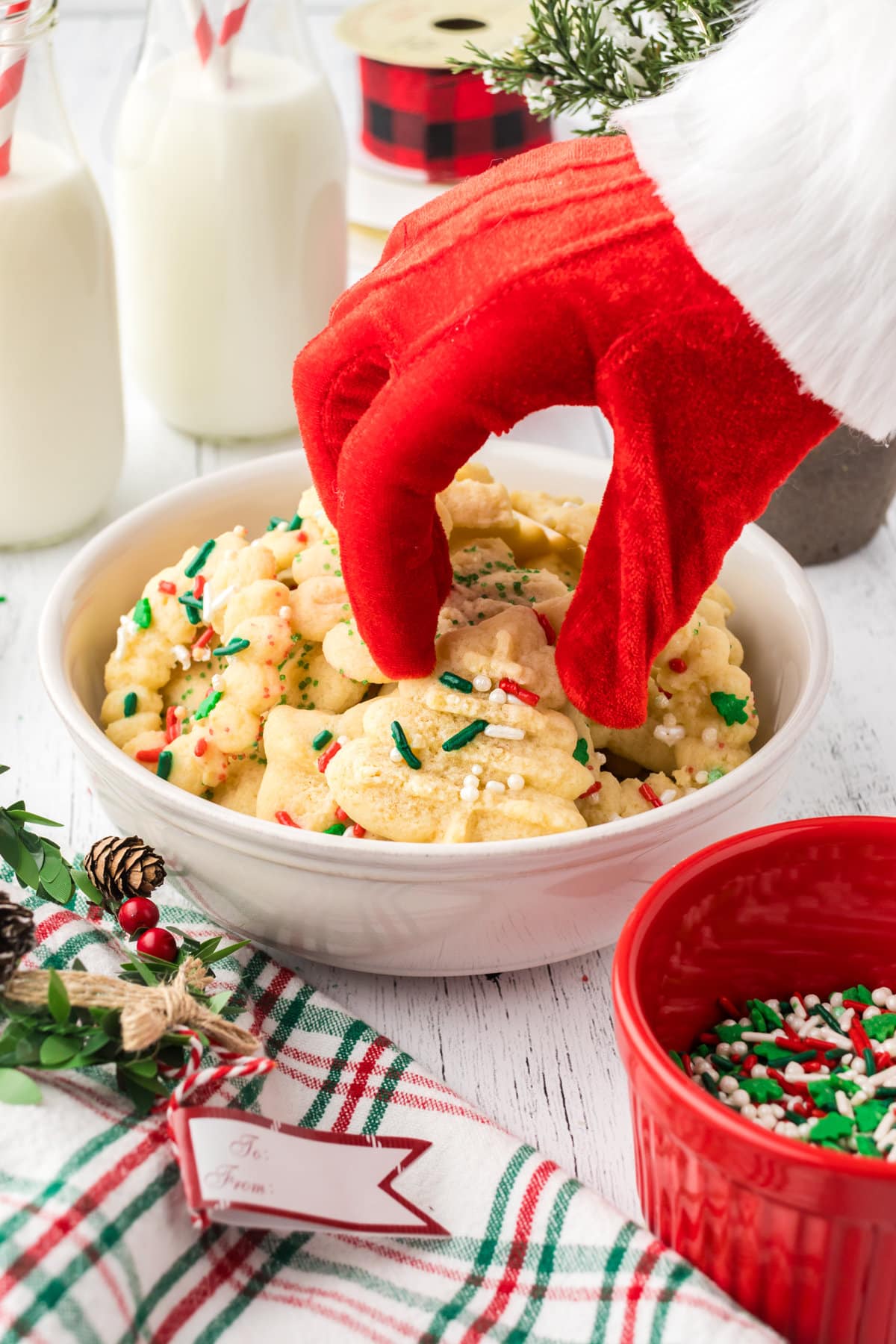 Santa's red glove reaching into a bowl full of sprinkled Spritz cookies.