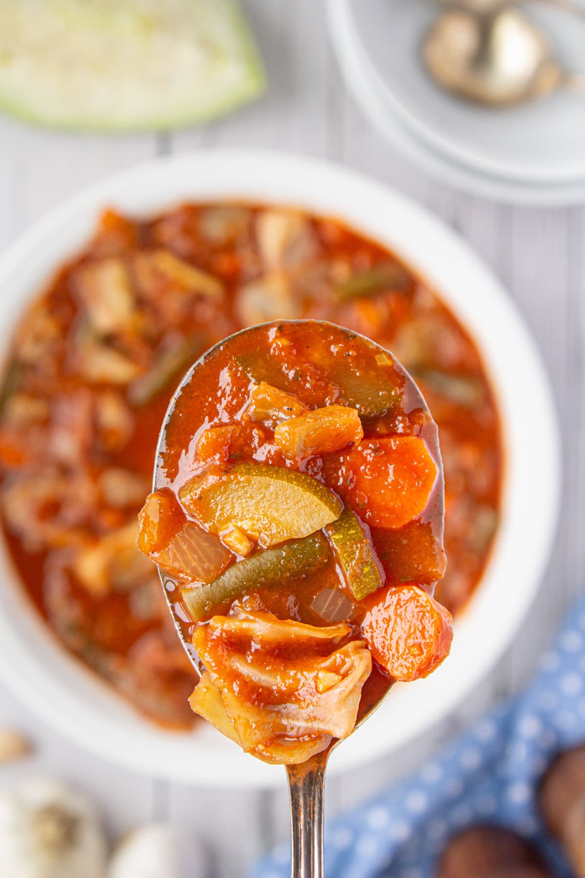 A ladle of cabbage soup—red broth filled with veggies such as carrots and onions.