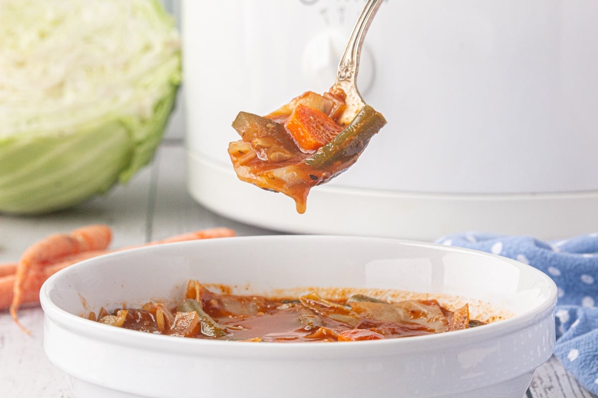 A spoon of 0-point Weight Watcher's cabbage soup hovers over a dinner bowl.