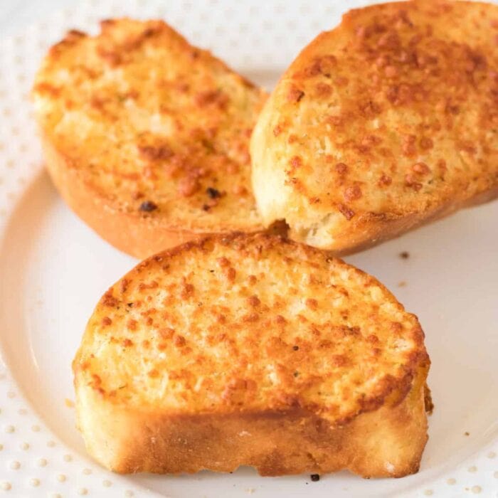 Closeup of golden brown, buttery pieces of garlic bread on a white plate.