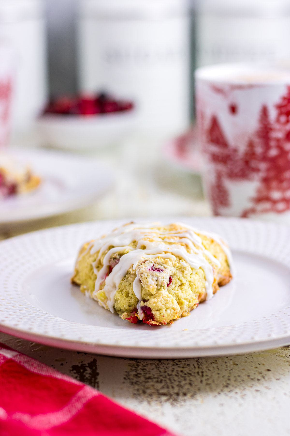 A close-up photo of a glazed cranberry scone on a white plate.