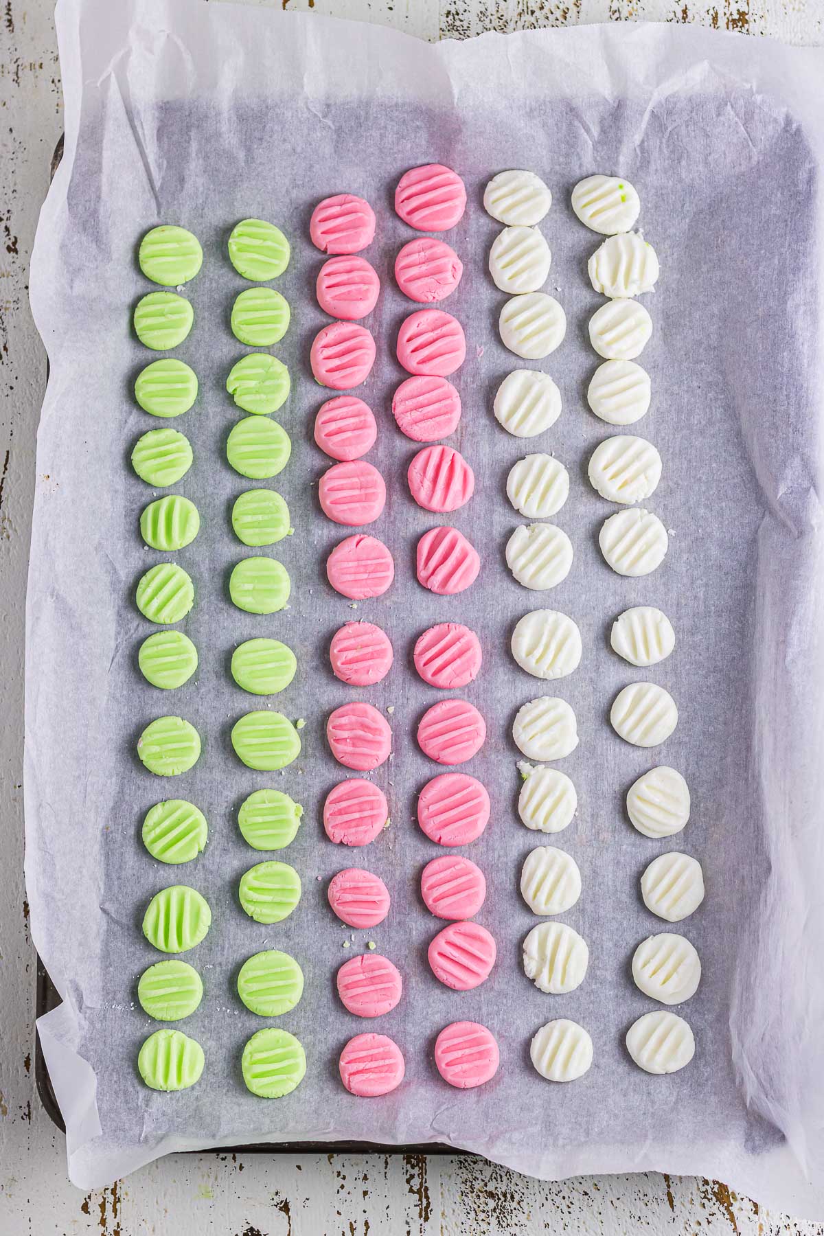 Green, pink, and white cream cheese mints on a parchment paper lined baking sheet.