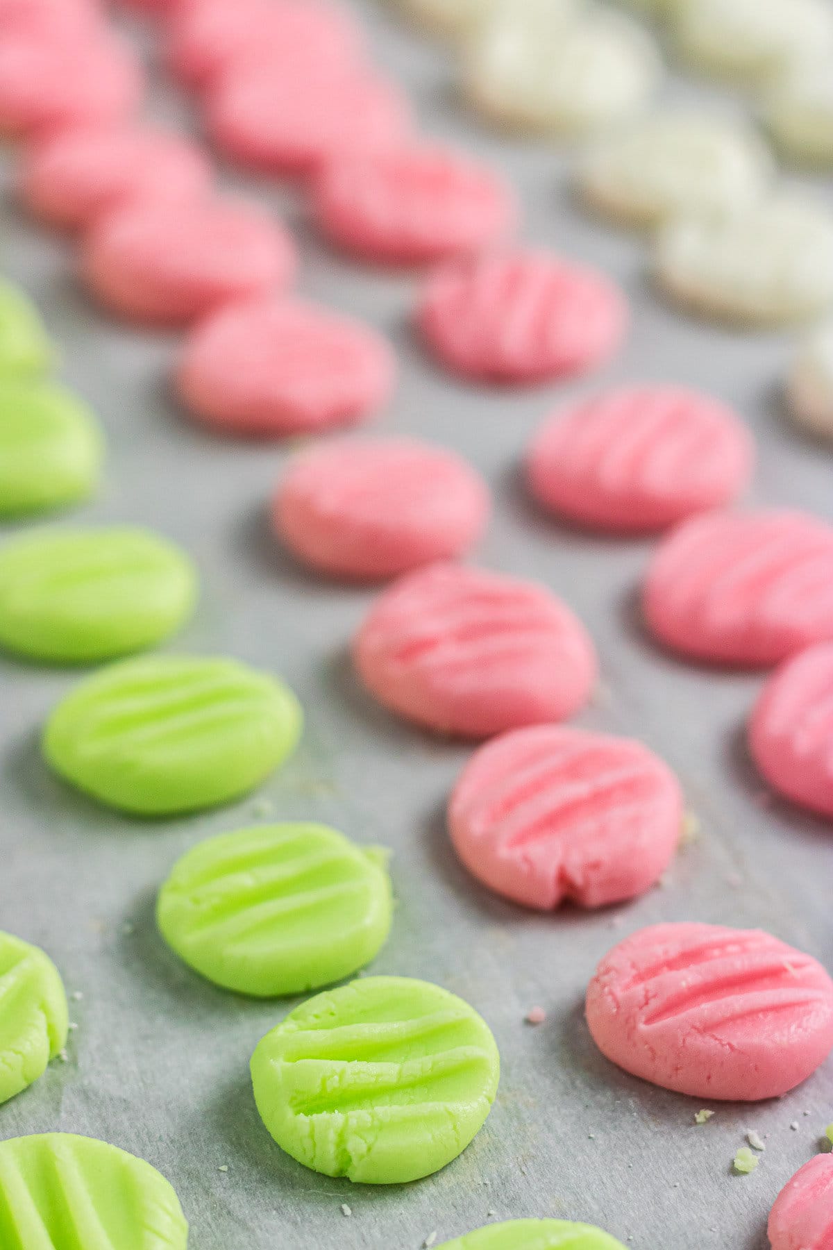 An up-close photo of green and pink mints on parchment paper.