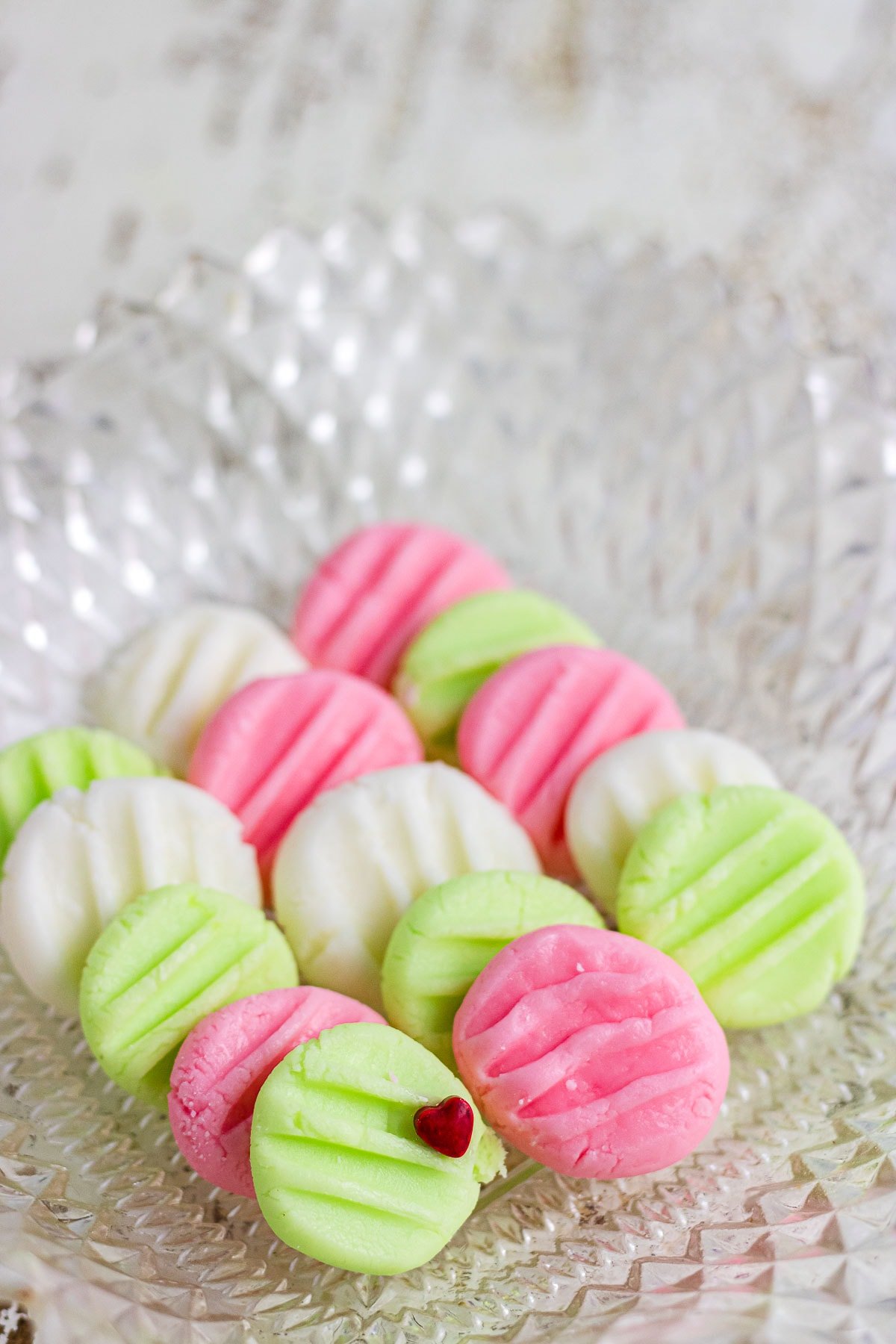 An up-close photo of pink, green, and white cream cheese butter mints in a decorative glass dish.