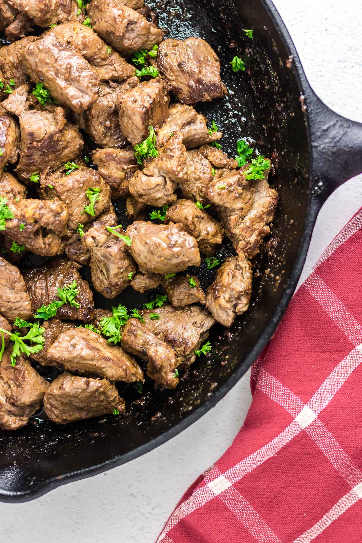 A skillet full of garlic butter steak tips with parsley sprinkled on top.