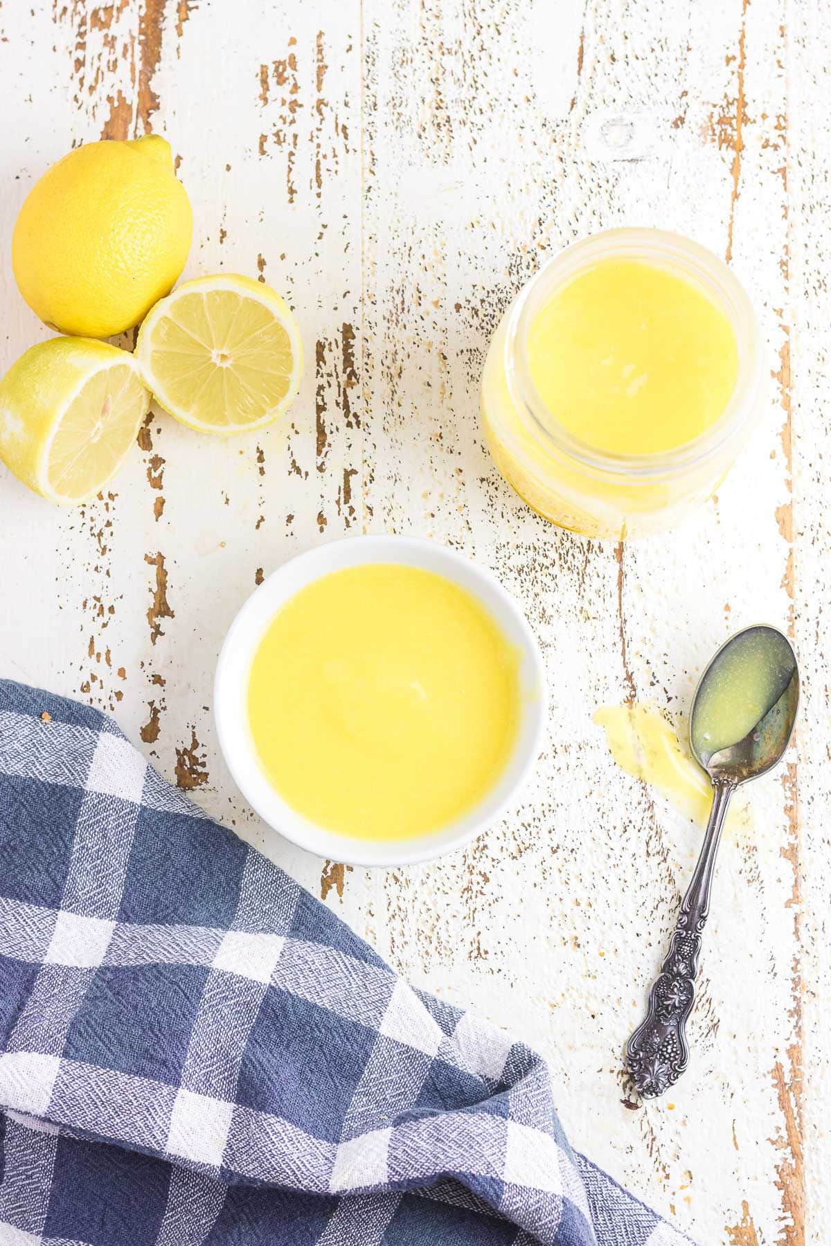 An overhead photo of a bowl and jar of lemon curd next to sliced lemons.