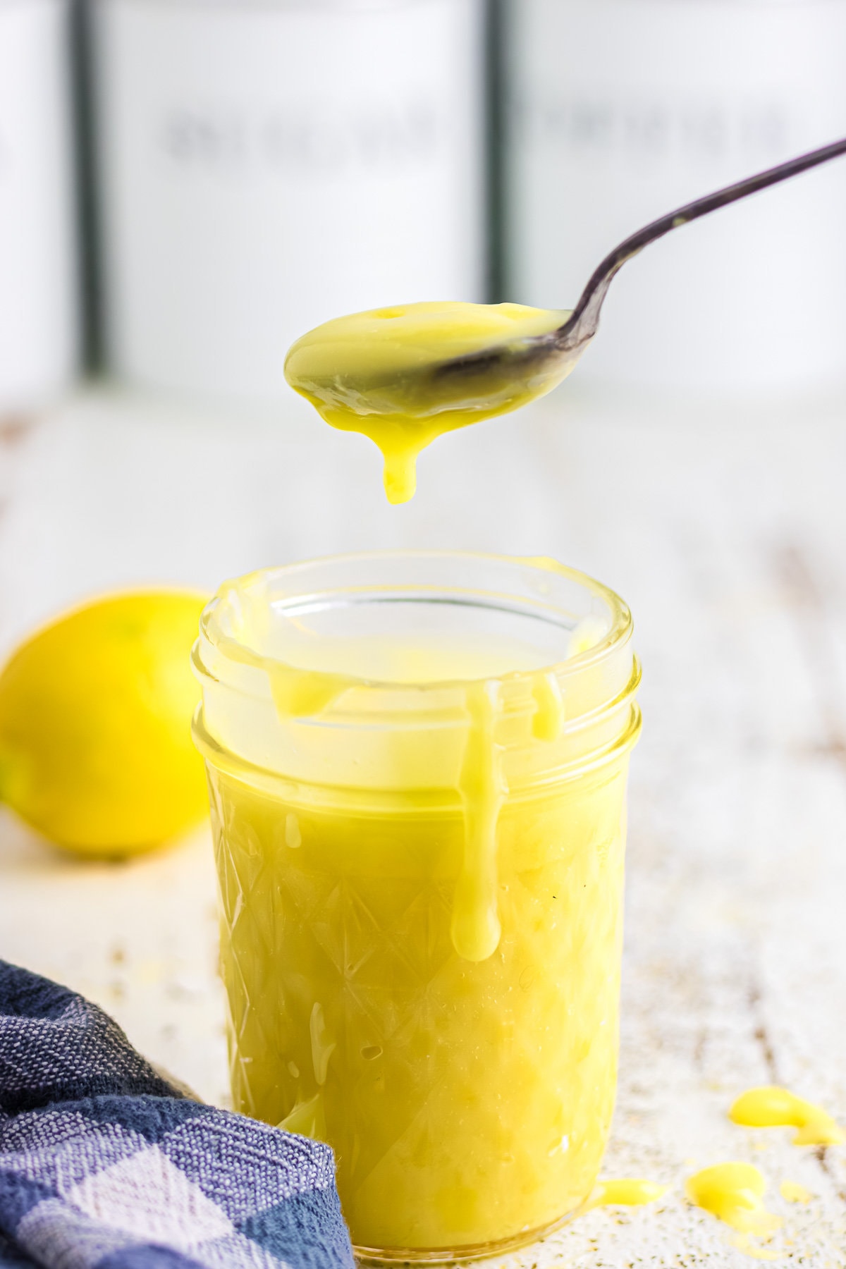 An up-close view of a mason jar filled with bright yellow lemon curd and a spoon scooping some out.
