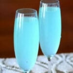 two champagne flutes with light blue cocktail inside.