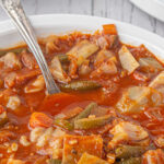 A closeup of a bowl of cabbage soup with a spoon in it. A title text overlay is on top of the image for Pinterest.