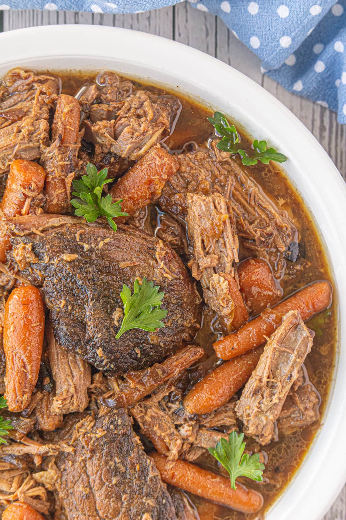 Rump roast with carrots and parsley in a white serving dish.