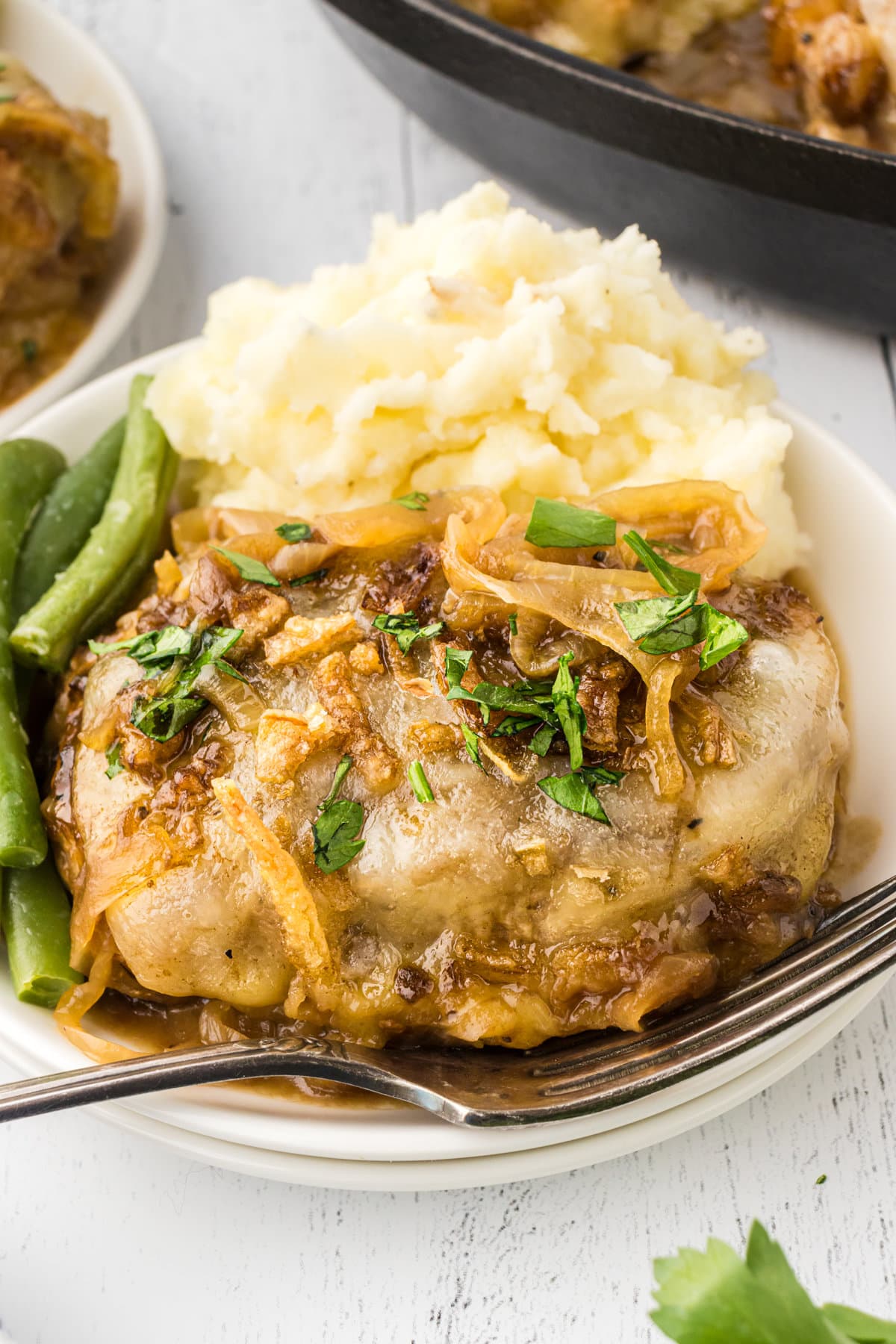A close-up photo of a cheesy pork chop topped with caramelized onions.