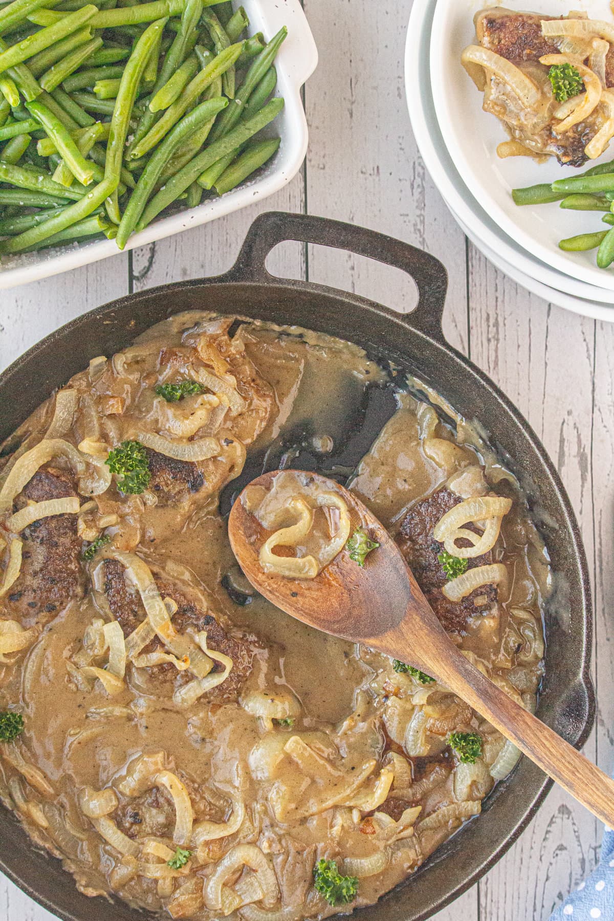 A skillet with gravy-covered liver and onions next to a plate of green beans.