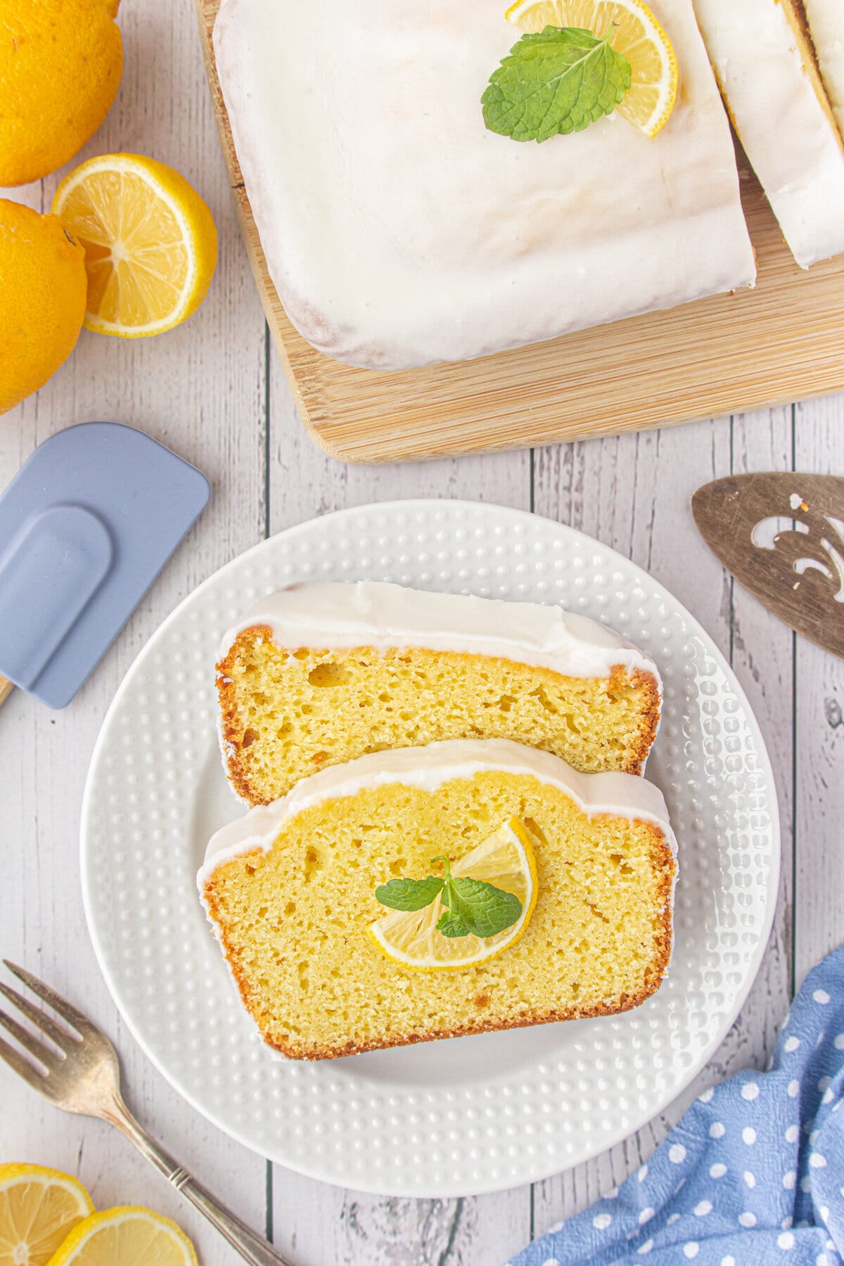 Two slices of iced lemon loaf on a white plate.