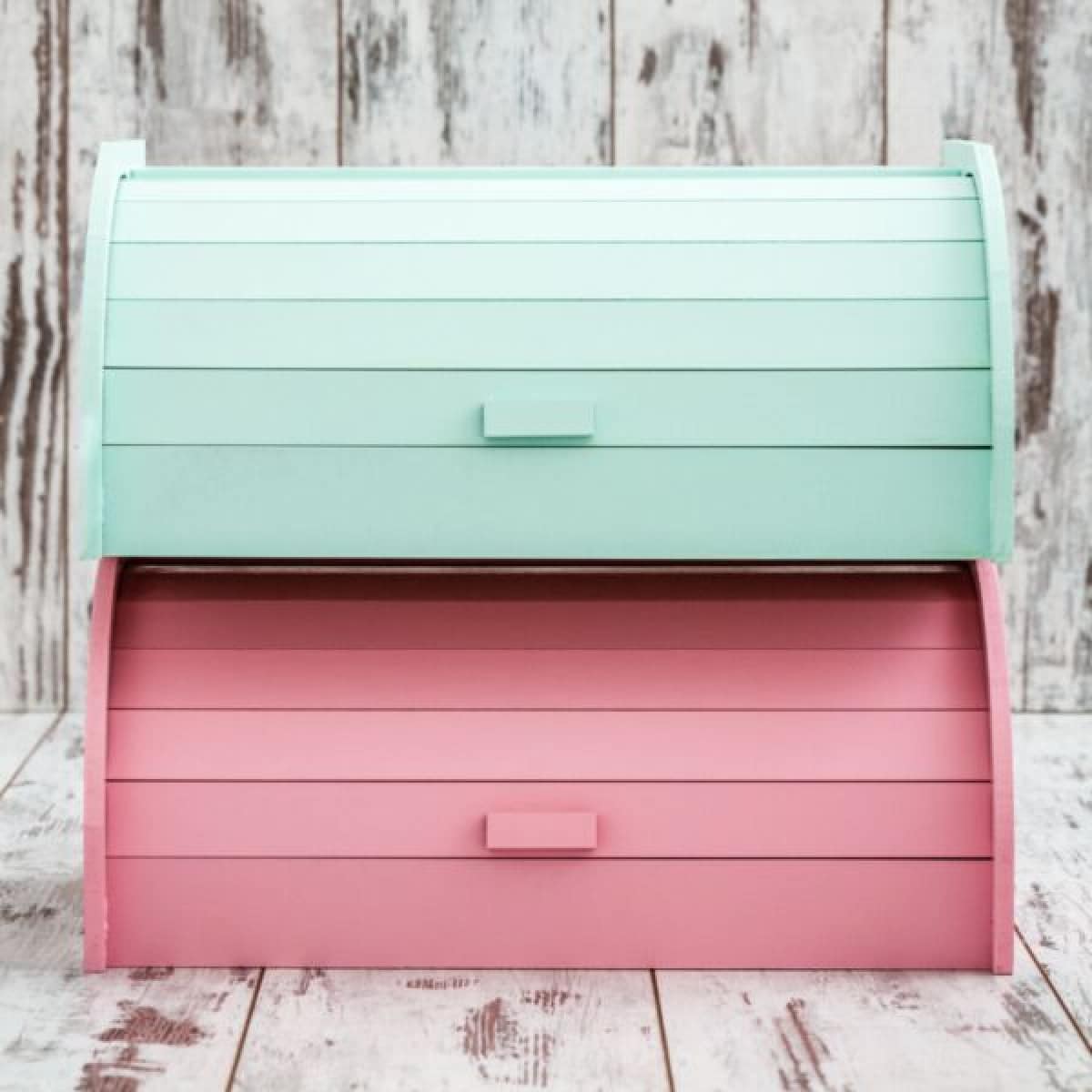 An aqua colored wooden bread box stacked on top of a pink wooden bread box.