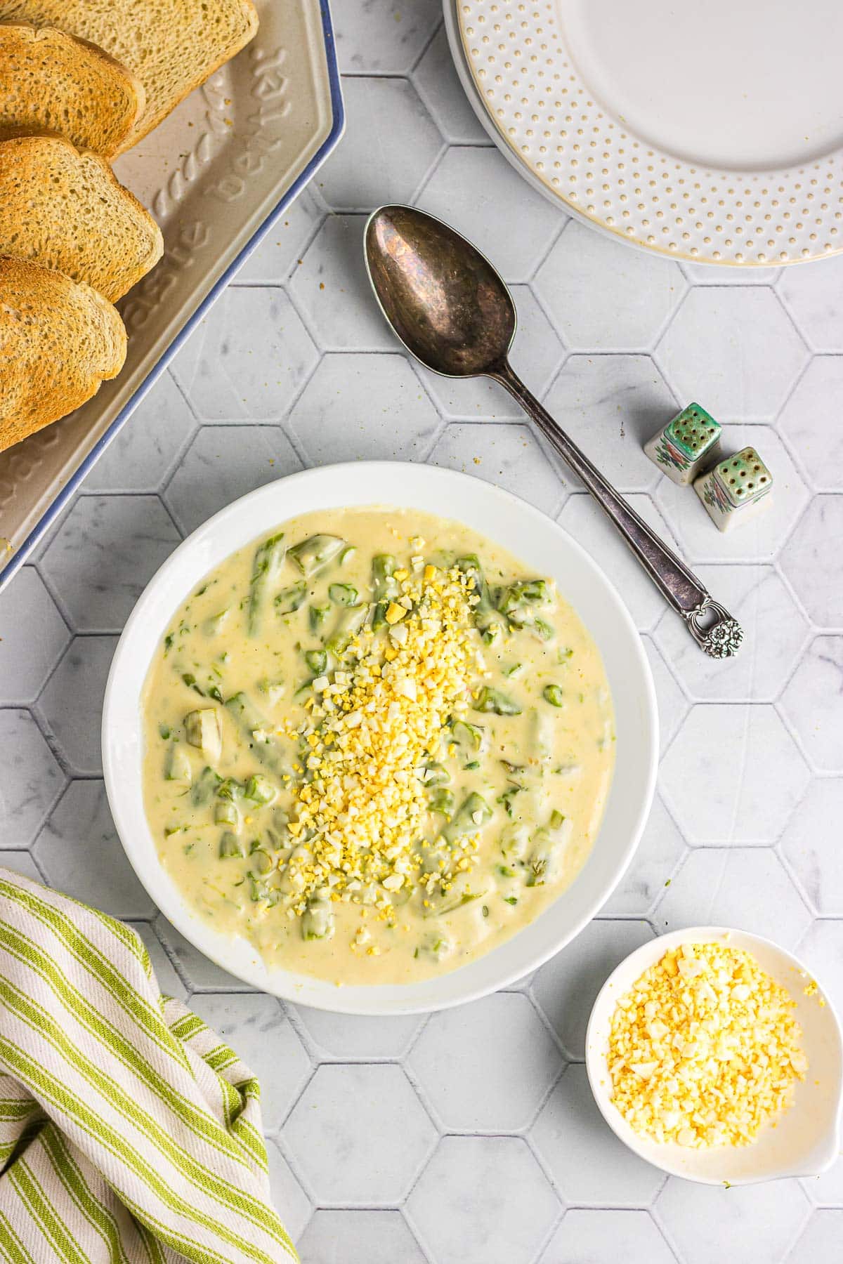 A bowl of creamed asparagus next to bread and crumbled hard-boiled egg.