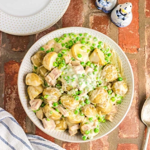 Creamed peas and potatoes in a white bowl sitting on a brick surface.