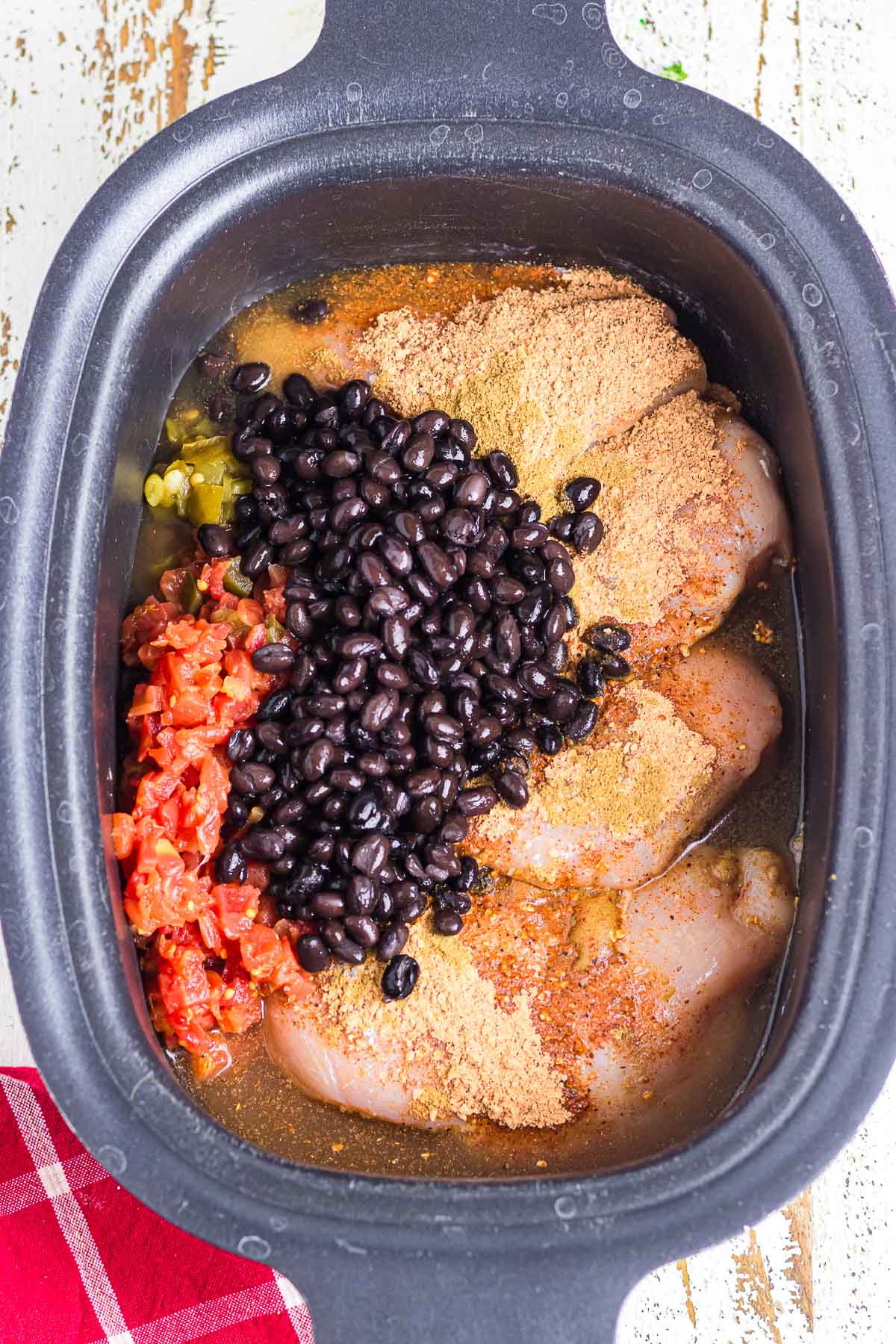 A crockpot filled with chicken, tomatoes, beans, and seasoning.