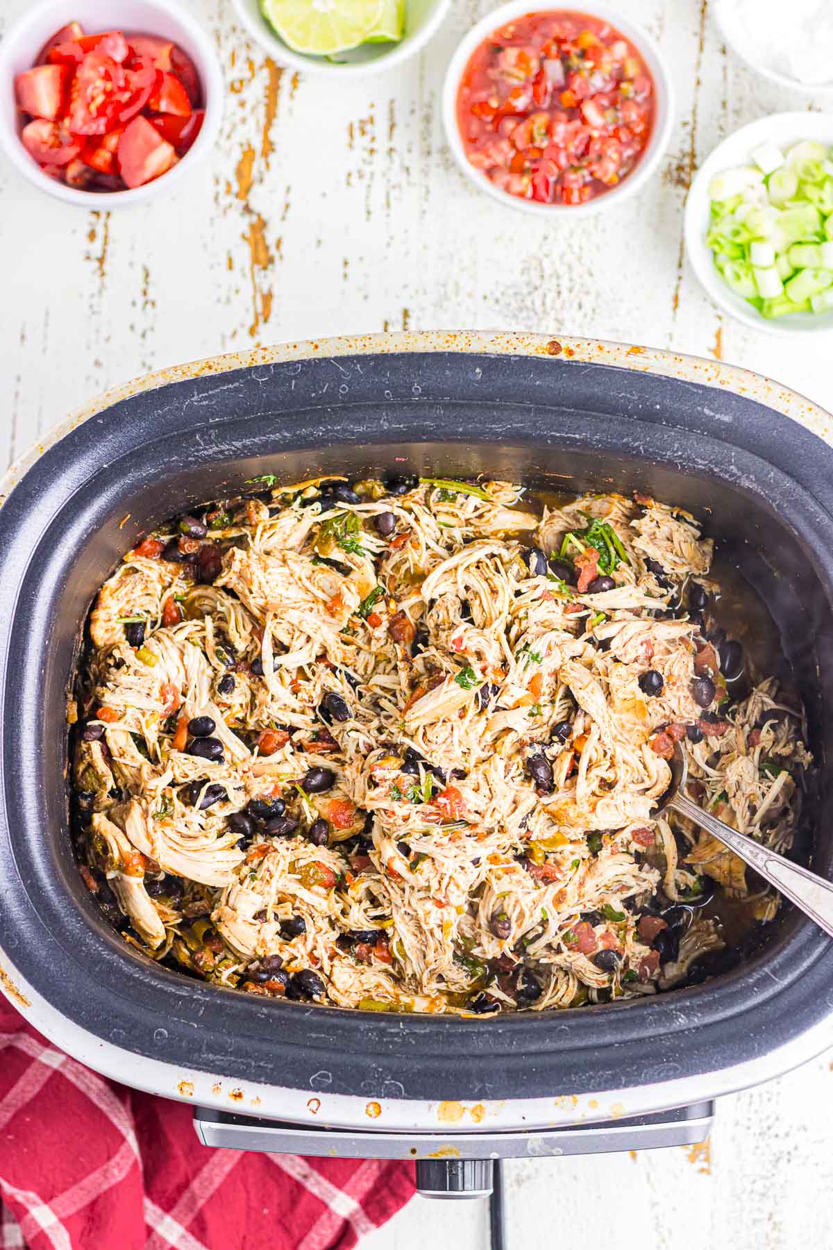A crockpot filled with cooked and shredded chicken, black beans, and tomatoes.