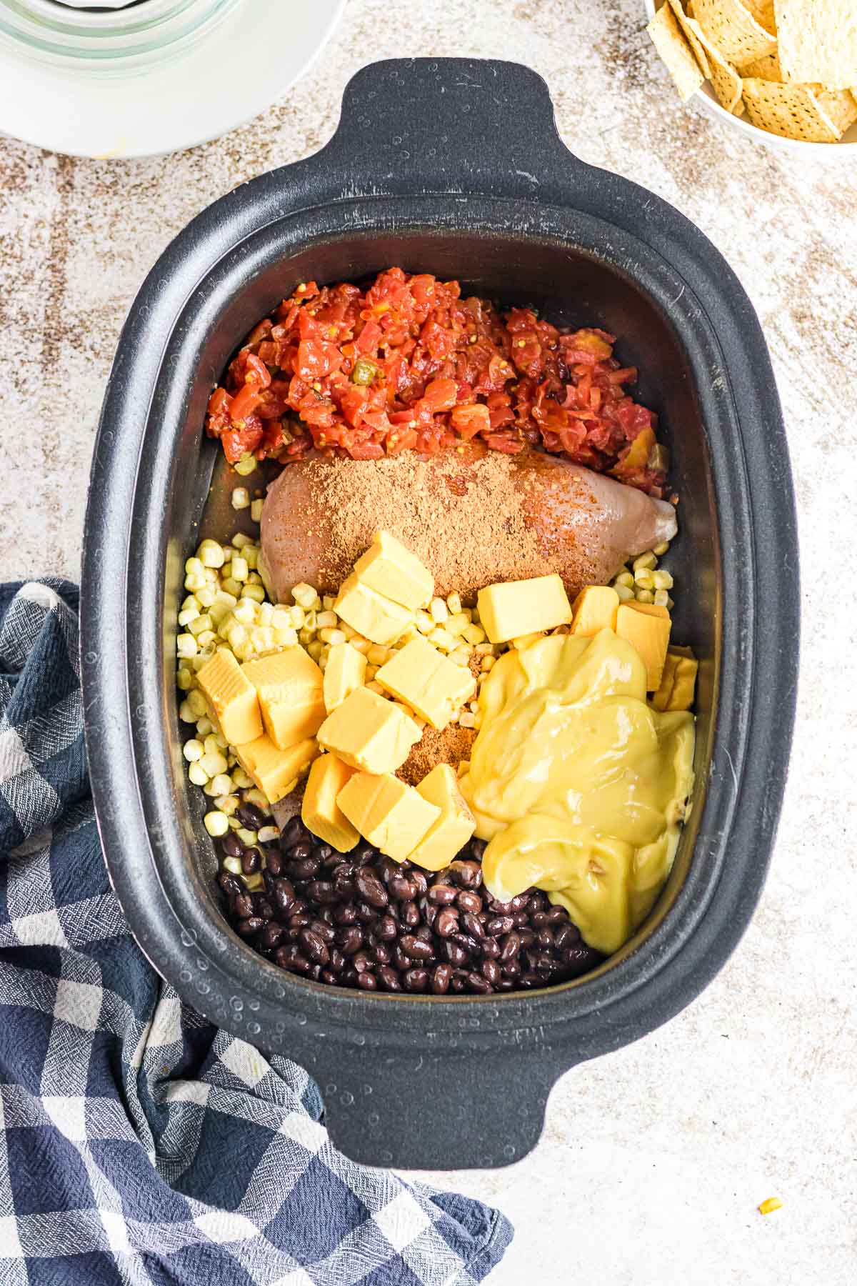 A crockpot filled with chicken, tomatoes, corn, cheese, and beans.