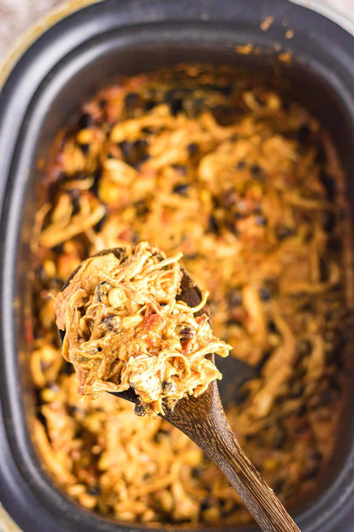 A scoop of chicken nacho dip on a spoon that's hovering over the crockpot.