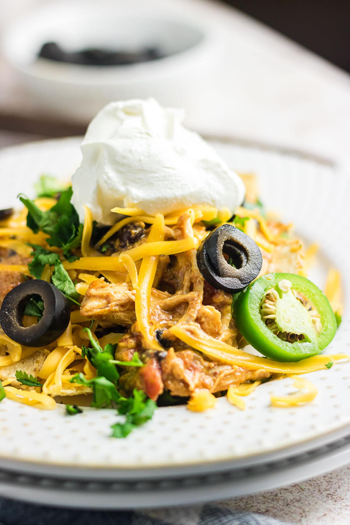 An up-close photo of creamy chicken nachos on a white plate topped with sour cream.