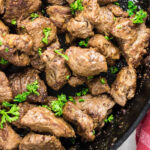 Garlic butter steak tips in a cast iron pan garnished with bright green chopped parsley.