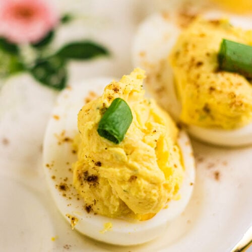 Closeup of a creamy deviled egg with a slice of green onion on top.