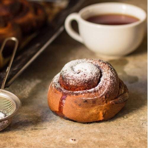 A cinnamon roll placed near a cup of coffee.