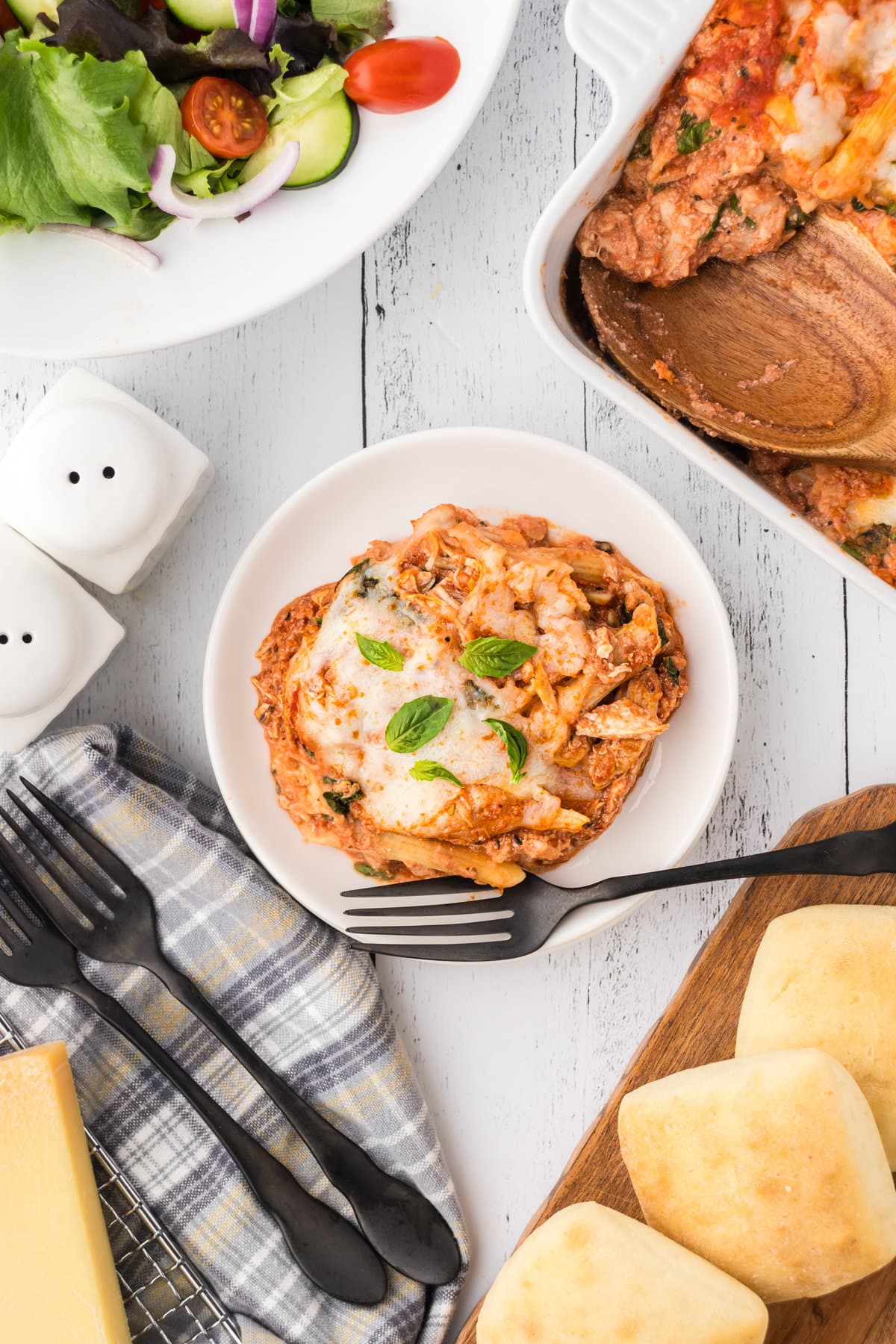 Ricotta chicken pasta in a dinner bowl next to rolls and a salad.