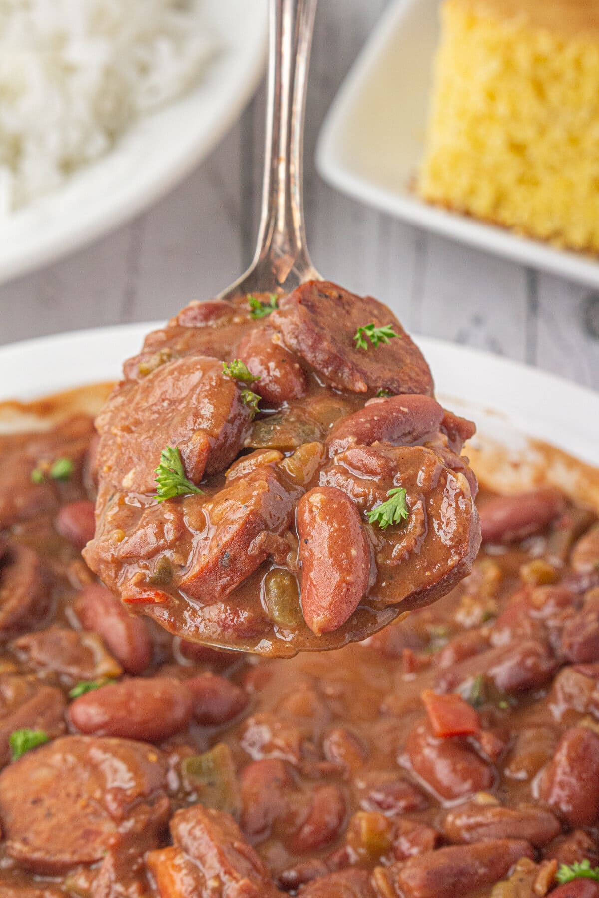 An up-close photo of a spoon of Southern red beans and sausage with rice in the background.
