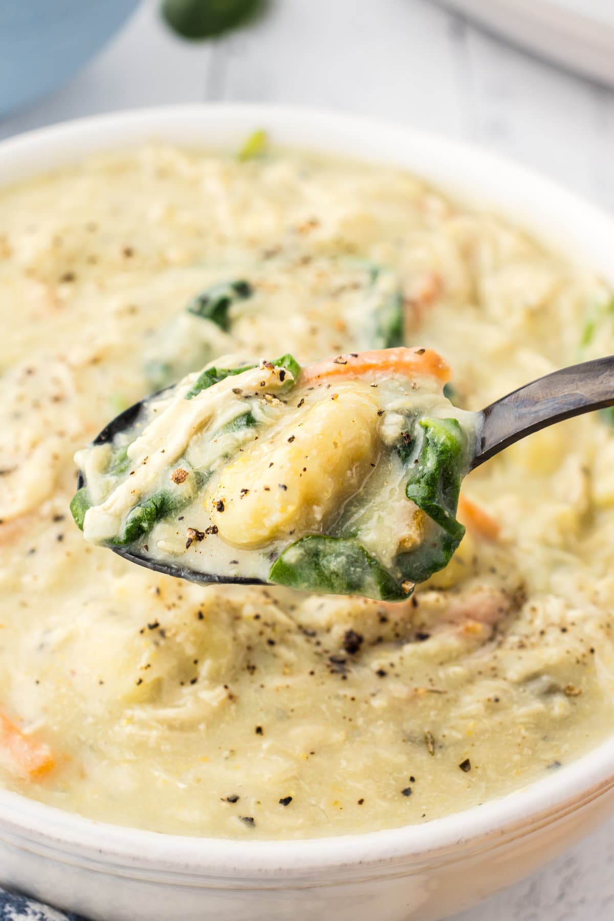 A spoon of slow cooker chicken gnocchi soup hovered over a dinner bowl with more soup.