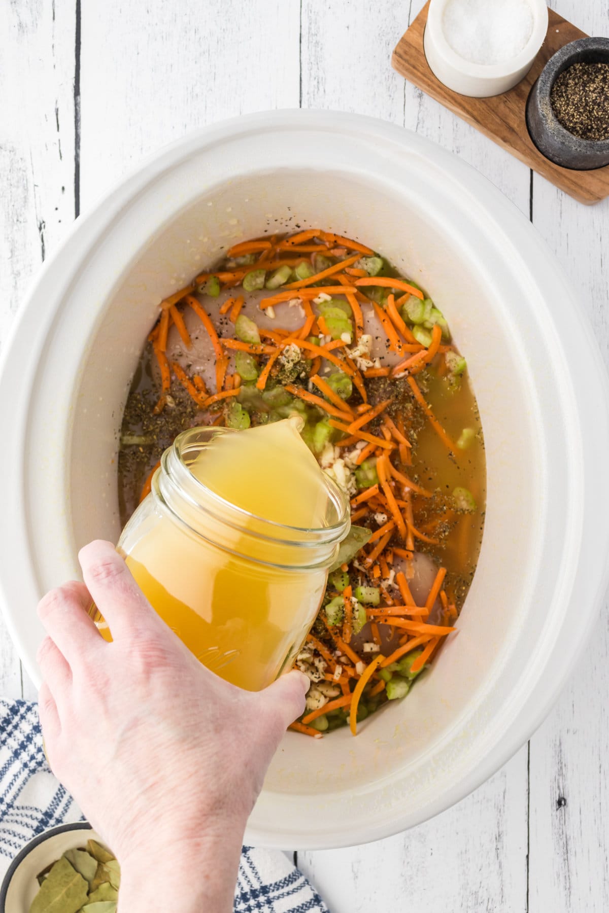 Adding stock to a crockpot with the other raw ingredients.